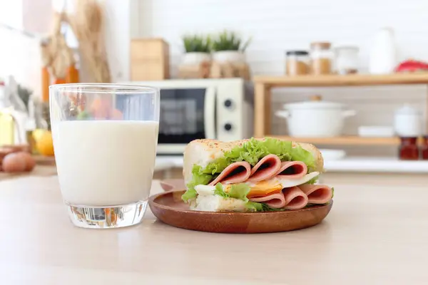 Glass of fresh milk and sandwich homemade on wooden table with blur modern cozy kitchen background. Eating healthy food breakfast in the morning, protein calcium rich food are essential for healthy.