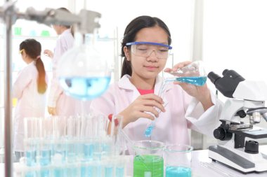 Laboratuvar önlüklü sevimli genç bilim kızı fen deneyleri yapıyor. Öğrenci kız okul laboratuarında kimya okumak için ekipman kullanıyor. Mutlu çocuk eğlenceli bir deney yapıyor. Çocuk fen eğitimi öğreniyor.