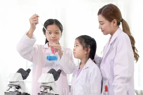 Two happy young scientist girls in lab coat use lab equipment for study in school laboratory. Asian female teacher teaches schoolgirl children to do science experiments. Kid learning science education