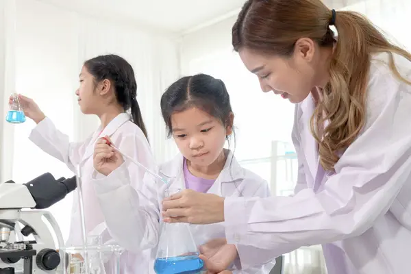 Happy young scientist girls in lab coat use lab equipment for study in school laboratory. Asian female teacher teaches schoolgirl children to do science experiments. Kid learning science education