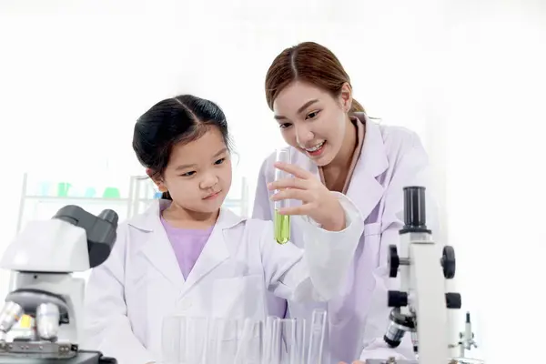 Happy young scientist kid girl in lab coats using lab equipment for study in school laboratory. Asian female teacher teaching schoolgirl child to do science experiments. Kid learning science education