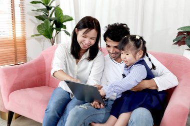 Oturma odasında mutlu bir aile, annesi ve babasıyla birlikte oturma odasında tablet kullanan tombul bir kız çocuğu. Çocuk evde ailesiyle çevrimiçi vakit geçiriyor. Çocuk, anne ve baba evde..