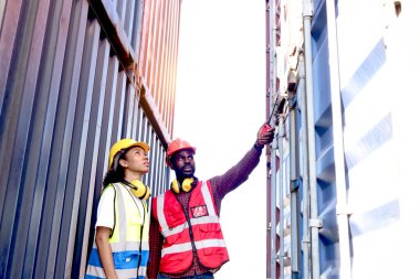 İki endüstriyel Afrikalı mühendis ve kadın güvenlik yeleği ve miğfer giyip lojistik kargo konteynerinde birlikte çalışıyorlar..