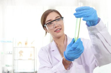 Laboratuvar önlüklü, güvenlik gözlüklü, yeşil kimyasallı test tüpü tutan Asyalı güzel bir bilim kadını. Araştırmacı araştırma için bilimsel deney yapmak için ekipman kullanır. Kadın bilim alanında çalışıyor..