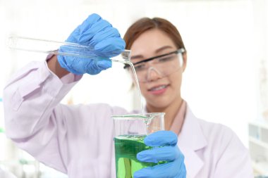 Laboratuvar önlüklü, güvenlik gözlüklü, bilim deneyi yapmak için deney tüpünden deney tüpüne kimyasal döken bilim adamı kadının elleri. Araştırmacı bilim alanında çalışan bir kadın için ekipman kullanıyor.