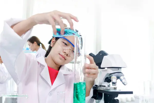 可爱的年轻科学家女学生穿着实验室外套和安全眼镜 做科学实验 女学生使用实验室设备在实验室学习化学 儿童学习科学教育 图库照片
