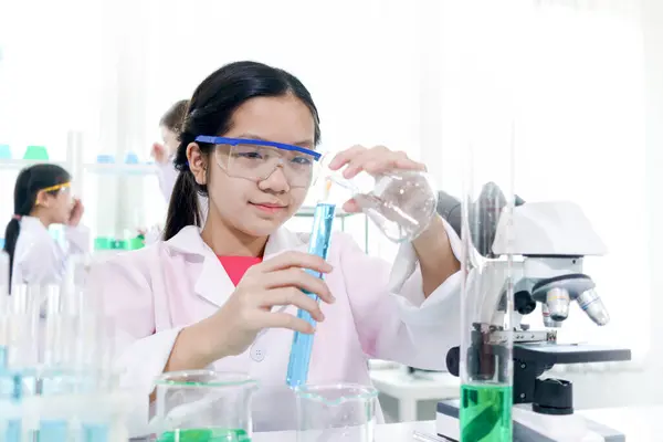 可爱的年轻科学家女学生穿着实验室外套和安全眼镜 做科学实验 女学生使用实验室设备在实验室学习化学 儿童学习科学教育 图库图片