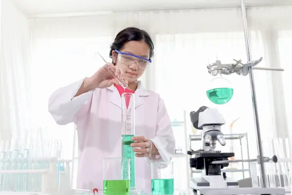 可爱的年轻科学家女学生穿着实验室外套和安全眼镜 做科学实验 女学生使用实验室设备在实验室学习化学 儿童学习科学教育 图库图片