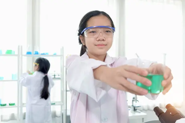 可爱的年轻科学家女学生穿着实验室外套和安全眼镜 拿着绿色化学烧杯 做科学实验 女学生在实验室学习化学 儿童学习科学教育 免版税图库图片