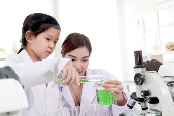 快乐的年轻科学家小女孩穿着实验室外套 用实验室设备在学校实验室学习 亚洲女教师教女学生做科学实验 儿童学习科学教育 图库图片