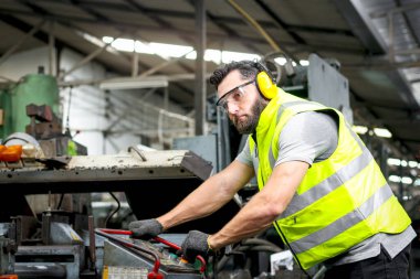 Fabrika fabrikasındaki motor denetimi sırasında kask ve güvenlik yeleği giyen erkek endüstriyel mühendis. İşçi endüstri işyerinde makine ile çalışan.