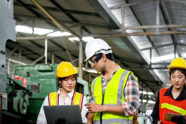 Bir grup sanayi ustabaşı mühendisi ve çelik yelek giyen işçiler makine motoru ve üretim sürecini kontrol etmek için fabrikanın önünden geçiyorlar. İş yerinde takım çalışması