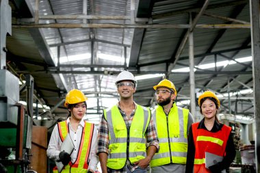 Bir grup sanayi ustabaşı mühendisi ve çelik yelek giyen işçiler makine motoru ve üretim sürecini kontrol etmek için fabrikanın önünden geçiyorlar. İş yerinde takım çalışması