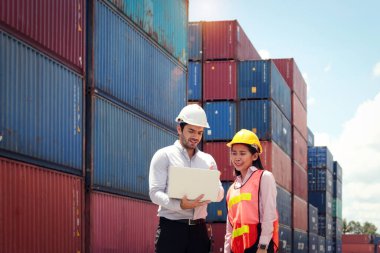 Lojistik kargo konteynır deposunda Asyalı kadın işçiyle sonuçları tartışırken elinde dizüstü bilgisayarla kasklı yakışıklı bir iş adamı. Foreman şantiyeyi inceliyor..