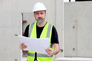 İnşaat alanında güvenlik yeleği ve miğferi olan ciddi bir usta mühendisin portresi. Stresli yaşlı mimar inşaat alanında çalışmayı düşünüyor.