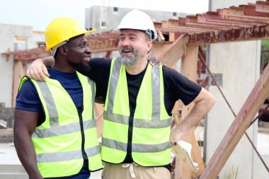 İş yerindeki mutlu ahenkli insanlar, gülümseyen beyaz ustabaşı ve Afrikalı mühendis inşaat alanında boyunlarına sarılıyorlar. Irk farklılıklarında sevgi ve saygı ten rengi, çeşitlilik