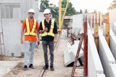 Güvenlik yeleği ve miğferi olan iki mutlu gülen işçi mühendis inşaat alanında çalışma alanını inceliyor. İnşaat alanının zemin katında birlikte çalışan bir mimar. İşçi inşaatı