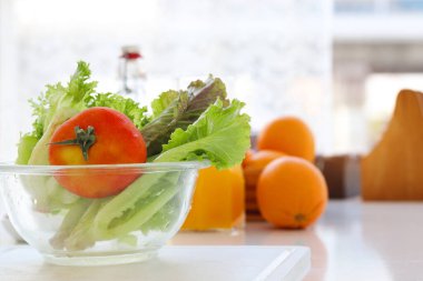 Ev mutfağında taze sebzeler ve salata kasesinde kırmızı domates. Lezzetli ve sağlıklı organik meyve ve sebzeler arka planda bulanık ev mutfağı.