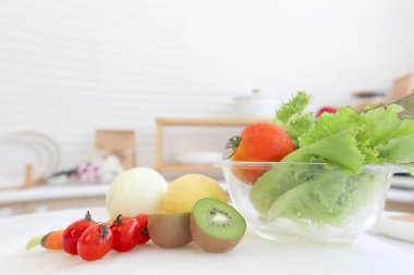 Ev mutfağında taze kivi, sebze ve salata kasesi var. Lezzetli ve sağlıklı organik meyve ve sebzeler arka planda bulanık ev mutfağı.