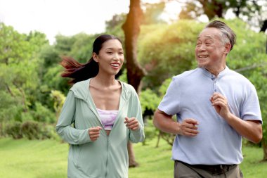 Yaşlı Asyalı bir adam sabah kızıyla parkta koşuyor. Mutlu büyükbaba yeşil bahçede torunuyla dışarıda egzersiz yapıyor. Aktif sağlıklı kıdemli, doğa geçmişi olan biri..