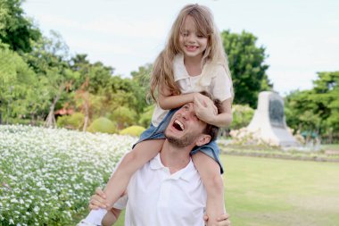 Babası tatlı kızını taşıyor, neşeli bir ebeveyn yaz tatilinde kızını parka götürüyor. Babam çocuklarla oynar ve güzel bahçede birlikte vakit geçirir. Mutlu aile dışarıda..