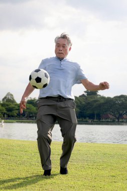 Yeşil halk parkında futbol oynayan mutlu Asyalı adam. Neşeli son sınıf öğrencisi en sevdiği futbol sporuyla dışarıda egzersiz yapmayı seviyor. Bahçenin arka bahçesinde aktif sağlıklı yaşlılar egzersizi.