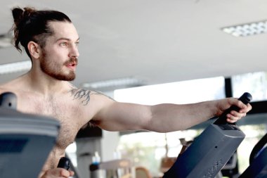 Spor aletleriyle spor yapan güçlü kaslı bir adam. Sporcu yakışıklı adam spor salonunda egzersiz için makineyi kullanıyor. Sağlıklı ve mükemmel bir vücut için tasarlanmış spor ve vücut geliştirme programı..