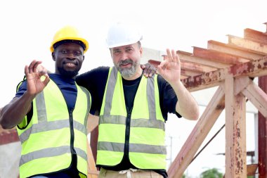 Mutlu uyum çeşitliliği çalışanı iş yerinde birlikte çalışıyor kıdemli ustabaşı ve Afrikalı mühendis boynuna sarılıyor inşaat alanında işaret parmağını gösteriyor. Farklılıklarda saygı