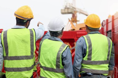 İnşaat alanının arkasında duran güvenlik yeleği ve miğferi olan bir grup mühendis. Mimarlık ekibi iş yerinde birlikte çalışıyor. İnşaat alanındaki yapıcının arkası.