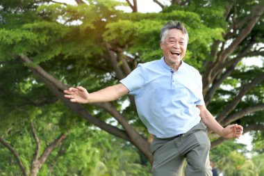 Neşeli, yaşlı Asyalı adam sabah parkta vücut esnetme için dans ediyor. Mutlu son sınıf öğrencilerinin yeşil bahçede eğlenceli egzersizleri var. Aktif sağlıklı yetişkin egzersizi, dışarıda doğa arka bahçesiyle dans etmek.