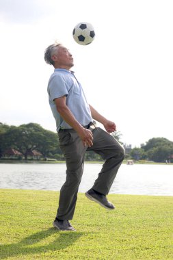 Yeşil halk parkında futbol oynayan mutlu Asyalı adam. Neşeli son sınıf öğrencisi en sevdiği futbol sporuyla dışarıda egzersiz yapmayı seviyor. Bahçenin arka bahçesinde aktif sağlıklı yaşlılar egzersizi.