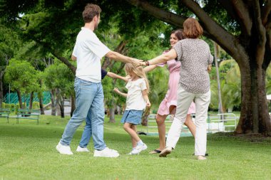 Neşeli aile el ele tutuşur ve yeşil çimlerin üzerinde dans eder. Baba, anne, kız, oğlan ve yaşlı büyükanne bahçede oynuyorlar. Mutlu çocuk, ailesi, parkta son sınıf öğrencisi..