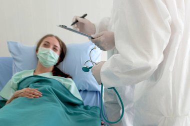 Hastalık tedavi odasında yüzü maskeli hasta hasta yatıyor. Koruyucu giysiler giyen doktor karantina hastanesinde tedavi görüyor. Tıbbi ekip hastaları bulaşıcı hastalıklarla tedavi ediyor.