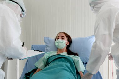 Hastalık tedavi odasında yüzü maskeli hasta hasta yatıyor. Koruyucu giysiler giyen doktor karantina hastanesinde tedavi görüyor. Tıbbi ekip hastaları bulaşıcı hastalıklarla tedavi ediyor.
