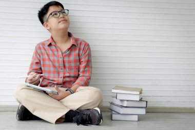 Sınıf zemininde otururken gözlüklü Asyalı çocuk kitap okuyor. İlkokul çocuğu portresi okulda öğrenim görüyor. Öğrenci zaman harcıyor. Çocuk ve eğitim