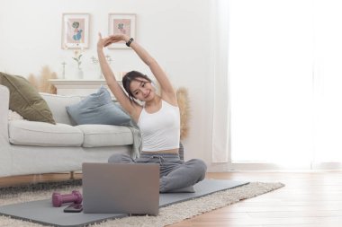 Asyalı kadın oturma odasında yoga minderinin üzerinde uzanıyor. Evde dizüstü bilgisayarda eğitim vdo 'sunu izlerken mutlu bir kadın antrenman yapıyor. Sportif kız egzersiz yapıyor. Sağlıklı ve spor hobisi