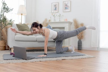 Asyalı kadın oturma odasında yoga minderinin üzerinde uzanıyor. Evde dizüstü bilgisayarda eğitim vdo 'sunu izlerken mutlu bir kadın antrenman yapıyor. Sportif kız egzersiz yapıyor. Sağlıklı ve spor hobisi