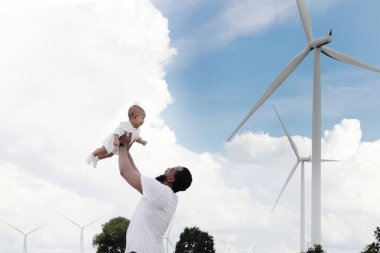 Mutlu Afrikalı aile rüzgar türbini çiftliğinde birlikte vakit geçiriyor. Babam tatlı bebekle oynuyor. Babası küçük çocuğu uçmak için taşıyıp kaldırıyor. Ekoloji alternatif yenilenebilir enerji teknolojisine sahip insanlar
