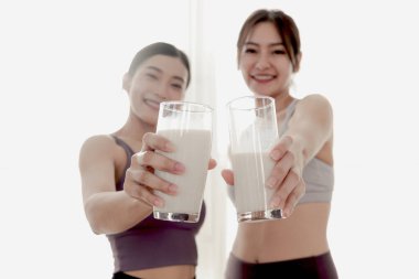 Sportif kız arkadaşın elinde iki bardak süt. Mutlu güzel Asyalı kadınlar idmandan sonra içmek için süt bardağı tutarlar. Vitamin ve kalsiyum açısından zengin yiyecekler. Sağlıklı yemek ve spor yaşam tarzı