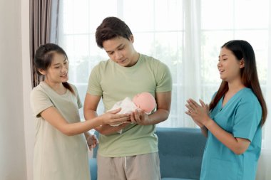 Mutlu Asyalı çift bebek taşımayı ve kaldırmayı kadın hemşireden öğreniyor. Hamile anne ve koca bebek kucağında oyuncak bebekle alıştırma yapıyorlar. Aile sağlık personelinden tavsiye alır.