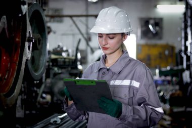 Koruyucu iş kıyafetleri olan endüstriyel mühendis kadın ve imalat fabrikasındaki belge dosyasındaki kaskları kontrol et. Güzel kadın işçi çelik endüstrisinde müfettiş olarak çalışıyor..