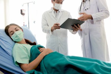 Enfeksiyon kapmış hasta için hastalık tedavi odası. Ameliyat maskesi takan hasta iki uzman doktorla aynı yatakta yatıyor. Doktor, hastanedeki karantina odasındaki hastalarla ilgilenin..