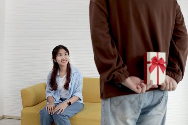 Arkasına hediye kutusu saklayan bir adam. Oturma odasında kutlama yapmak için sevgilisine yıldönümü hediyesi vermeye hazır. Mutlu Asyalı çift sürpriz yapar, aşk ve mutluluk. Sevgililer Günün kutlu olsun..