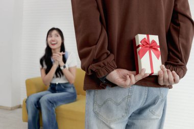 Arkasına hediye kutusu saklayan bir adam. Oturma odasında kutlama yapmak için sevgilisine yıldönümü hediyesi vermeye hazır. Mutlu Asyalı çift sürpriz yapar, aşk ve mutluluk. Sevgililer Günün kutlu olsun..