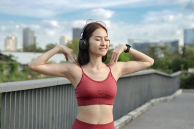 Spor giyimli kısa saçlı sporcu kız egzersiz yapmadan önce ısınmak için şehrin vücut kısmını esnetiyor. Mutlu gülümseme Asyalı kadın dışarıda spor yapıyor. Sağlıklı açık hava aktivitesi.