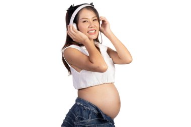 Mutlu gülümseyen Asyalı hamile kadının portresi kulaklık takan, beyaz arka planda büyük göbekli bir anne. Karnında müzik dinleyen hamile bir anne. Mutlu aile