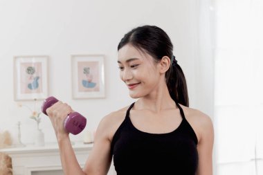 Asyalı güzel kadın evde dambılla egzersiz yapıyor. Gülümseyen genç atletik kadın vücudunu eğitmek için dambılını kaldırıyor. Sportif kızlar antrenman yapar. Sağlıklı spor hobi yaşam tarzı.
