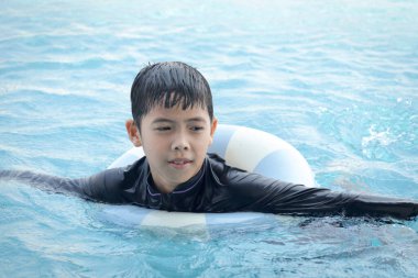 Yüzme yüzüklü mutlu Asyalı çocuk mavi suda yüzüyor. Yaz tatilinde açık havuzda şişme yüzükle oynayan rahatlatıcı çocuk. Hafta sonu havuzda yüzen neşeli çocuk.