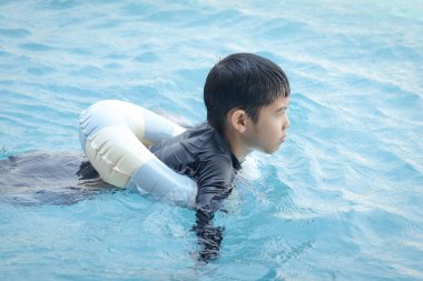 Yüzme yüzüklü mutlu Asyalı çocuk mavi suda yüzüyor. Yaz tatilinde açık havuzda şişme yüzükle oynayan rahatlatıcı çocuk. Hafta sonu havuzda yüzen neşeli çocuk.