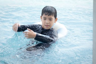 Yüzme yüzüklü mutlu Asyalı çocuk mavi suda yüzüyor. Yaz tatilinde açık havuzda şişme yüzükle oynayan rahatlatıcı çocuk. Hafta sonu havuzda yüzen neşeli çocuk.